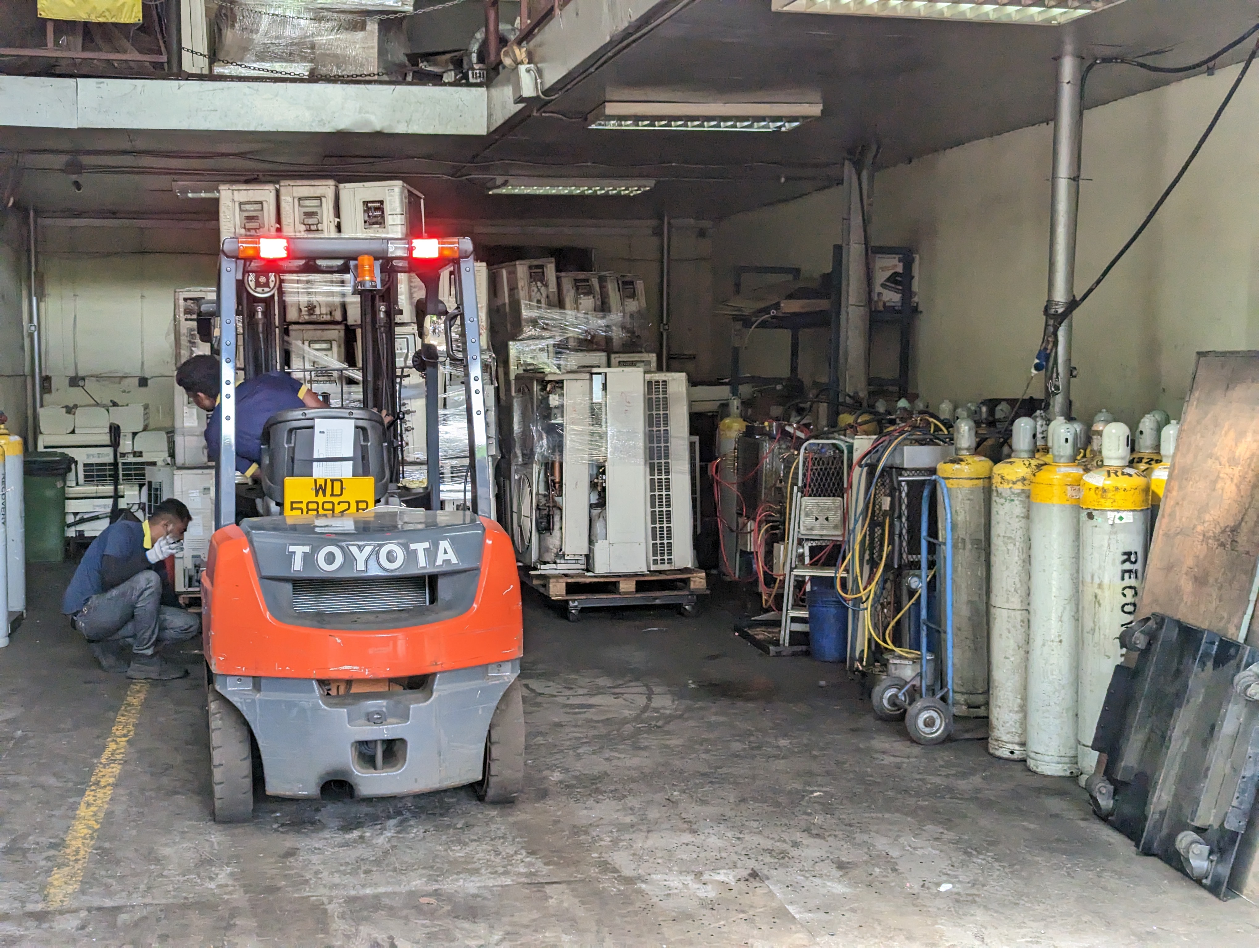 A forklift delivers a new bale of mini splits from which Cheng Hwa must recover refrigerant. The gray and yellow cylinders to the right contain recovered gases. One cylinder contains 125 pounds (58 kilograms) of refrigerant gas, equivalent to over 113 metric tons of carbon dioxide equivalent. Photo: Tilden Chao, 2023.